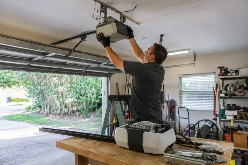 Person holding an overhead garage-door opener beside another opener and hardware on a workbench — Garage Door Opener Replacement, Peterborough