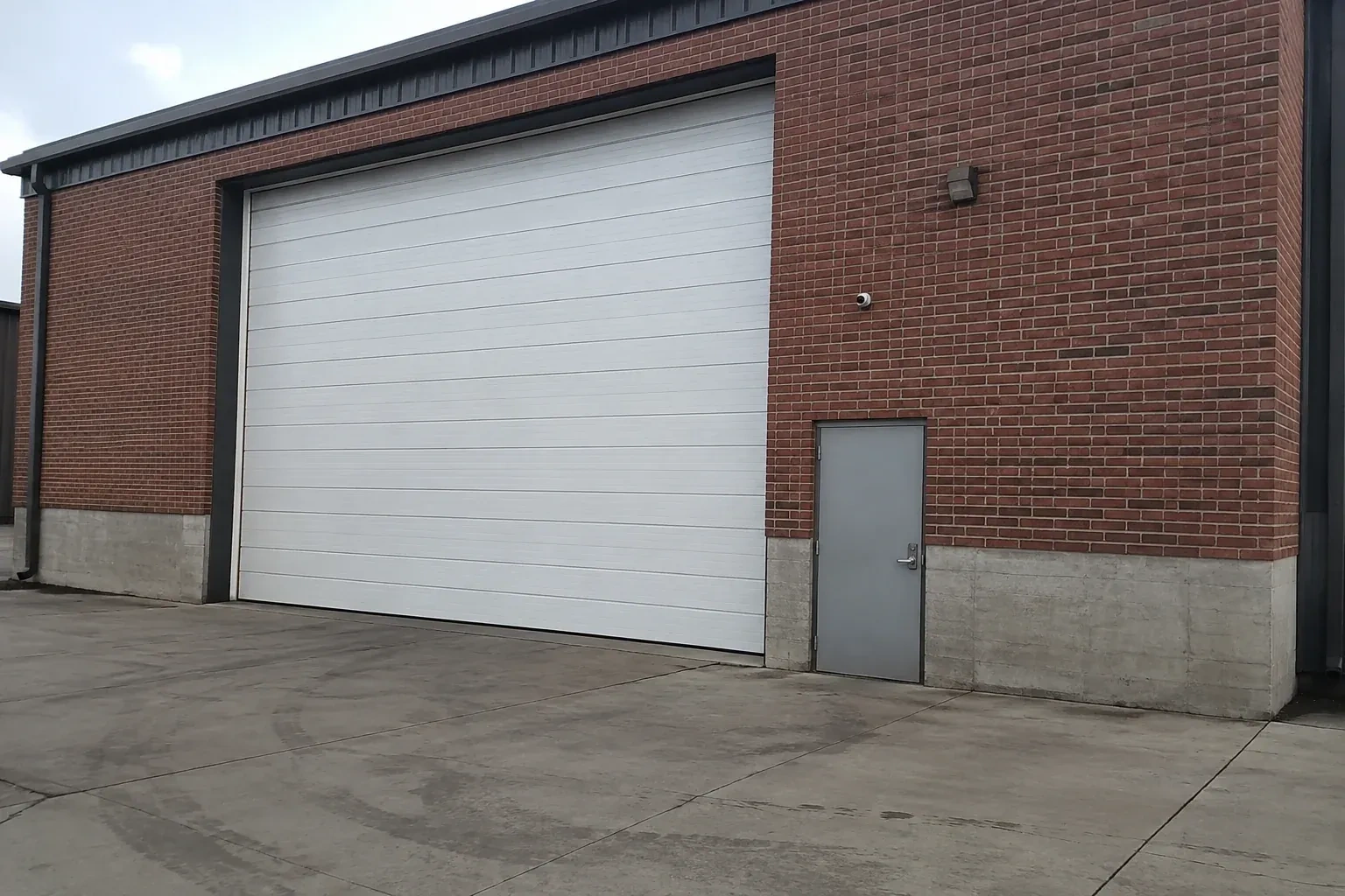 Tall closed sectional loading door beside a personnel door at a brick unit. — Commercial Sectional Door Repair, Peterborough